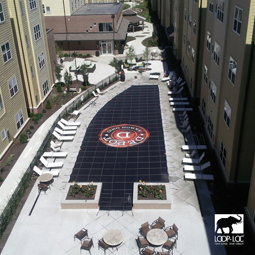 A commercial in-ground pool is closed for the winter and has a black pool cover with a red logo that says DEPOT in Akron, Ohio.